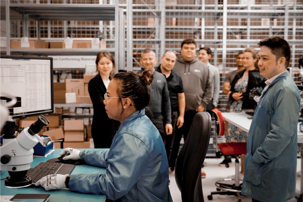 grupo observando a una mujer con una bata de laboratorio azul en la computadora
